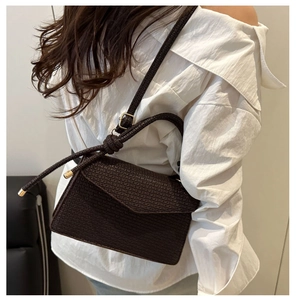 Détail du sac bandoulière marron foncé tressé avec boucle dorée sur un mannequin en blanc
