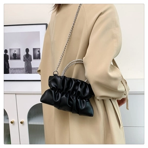Detail of black pleated cloud bag with rhinestone handles and silver chain on beige coat