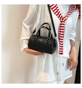 Primer plano de bolso cilíndrico negro con acolchado de corazones y lazo plateado elegante