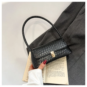 Detail of crocodile embossed texture on a black shoulder bag with gold metal buckle