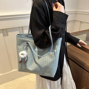 Detail of light blue woven tote bag with a fun plush charm and slim shoulder straps