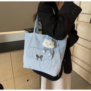 Detail of light blue tote bag with metallic butterfly buckle and white plush charm