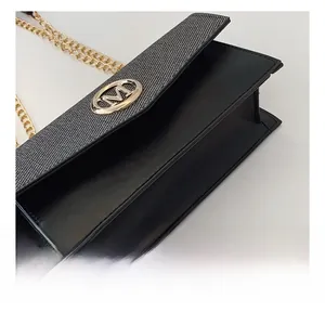 Detalle de bolso de cuero negro con tela gris, hebilla dorada logo M y cadena fina