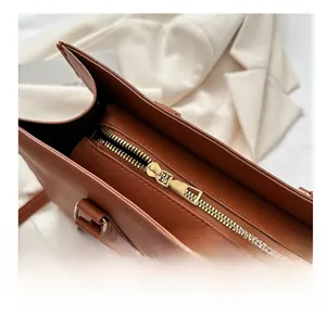 Close-up of smooth golden metal zipper and textured brown Saffiano leather on business tote
