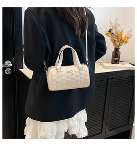 Model wearing a cream cylinder crossbody bag with heart quilting and bow detail