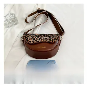 Brown saddle bag with leopard print flap and wide strap shown with a phone for scale