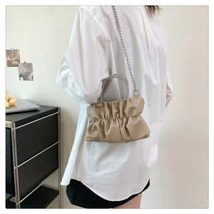 Close-up of khaki pleated cloud bag featuring rhinestone handles and metal chain strap
