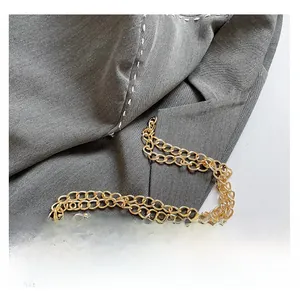 Detailed view of the gold metal chain strap on textured grey fabric with hand stitching
