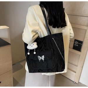 Rear view of a black tote bag with silver butterfly and plush cloud charm on a model