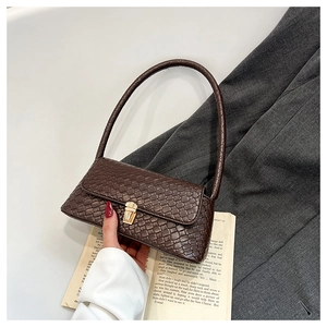Detail of dark brown baguette bag with crocodile texture and gold clasp on a blazer