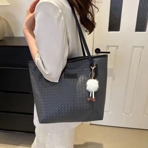 Detail of black woven tote bag featuring a plush charm on a textured faux leather surface