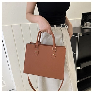 Detail of a brown PU leather tote bag with leaf-shaped metal ornament and long shoulder strap