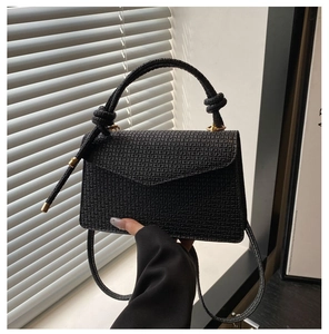 Détail d'un sac à main en cuir noir gaufré avec poignée à nœud et garnitures dorées