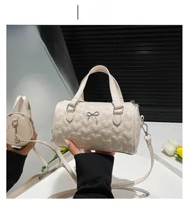 Detalle del bolso cilíndrico blanco crema con acolchado de corazones y lazo de metal