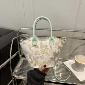Mint green floral embroidered bucket bag with leather handles in a casual indoor setting