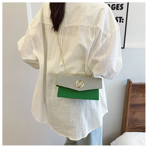 Detalle de bolso bandolera verde y gris con hebilla M dorada y correa de cadena