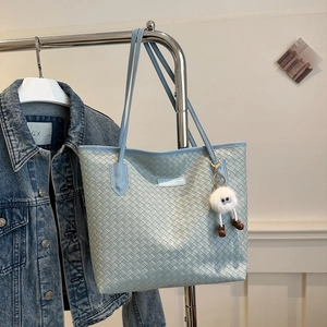 Detailed view of light blue woven tote bag with cute plush monster charm on metal hanger