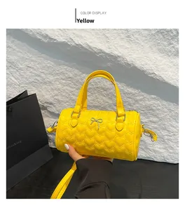 Vista detallada del bolso cilíndrico amarillo con acolchado de corazón y lazo