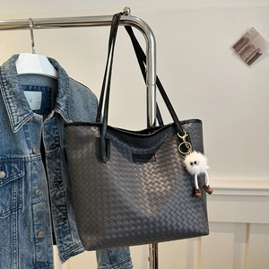 Detail of dark grey woven tote bag with plush charm and fashion label on blue denim background