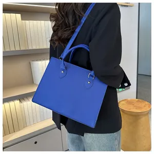 Detail of Klein blue commuter tote bag with gold hardware held by a model in black suit