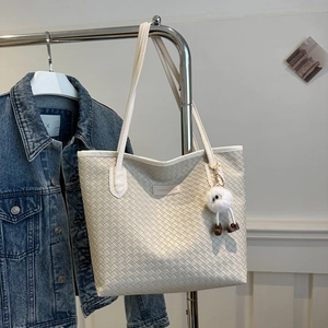 Detail of off-white woven tote bag with FASHION & BAGS label and plush monster charm
