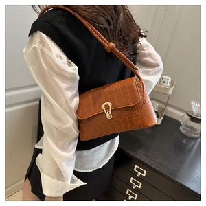 Brown crocodile-textured underarm bag with gold buckle shown on a model in a warm room