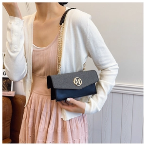 Detalle de bolso bandolera de cuero negro con solapa de tela gris y adorno M dorado