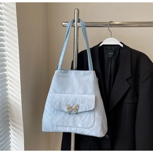 Close-up of light blue textured tote bag with a decorative silver metal butterfly buckle