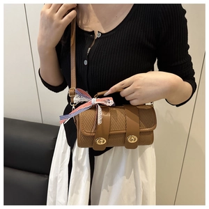 Détail du sac cylindrique tissé avec lanières en cuir, fermoir doré et nœud écossais