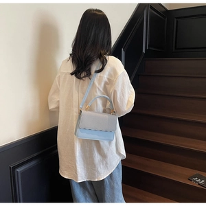 Close-up of light blue handbag featuring scalloped edges and woven texture on flap cover