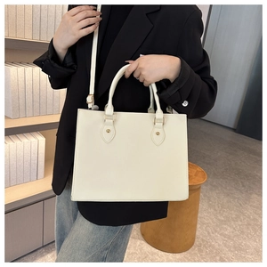 Close-up of cream leather tote bag featuring gold stud details and detachable shoulder strap