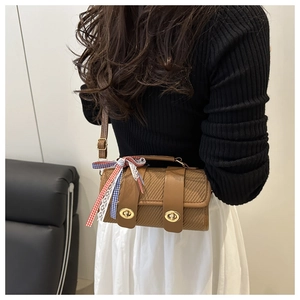Detail of a brown textured crossbody bag with gold clasps and a plaid ribbon charm