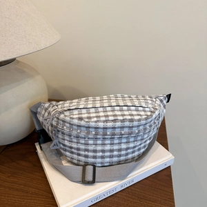 Gray and white checkerboard crossbody chest bag with adjustable strap on a book
