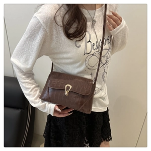 Gros plan sur un sac bandoulière marron foncé à texture crocodile et boucle dorée en forme de U