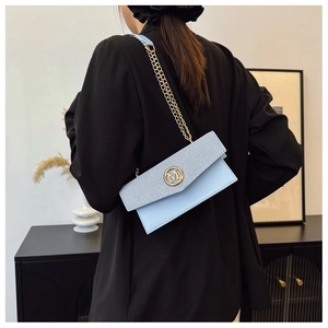 Détail du sac bandoulière bleu clair avec logo M et chaîne dorée sur modèle