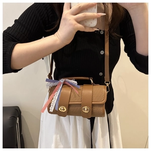 Detailed close-up of brown woven cylinder bag with leather straps and colorful ribbon