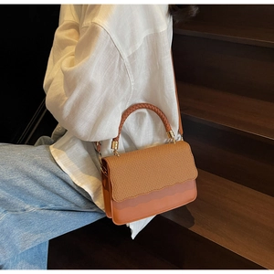 Brown shell bag with woven texture detail and metal buckle shown on a model's shoulder
