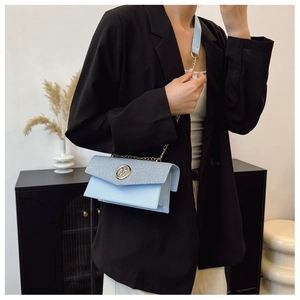 Détail du sac bandoulière bleu clair avec texture tissée et boucle logo M dorée