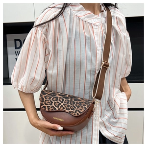 Detail of the leopard print saddle bag featuring a wide fabric strap and golden text