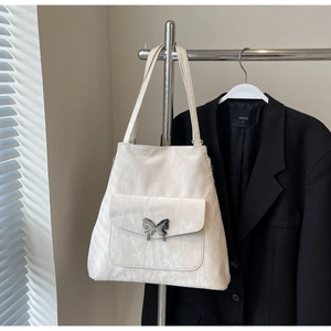 Close-up of off-white ruched tote bag featuring a silver metal butterfly buckle on pocket