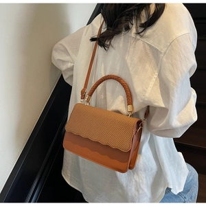 Detail of a brown crossbody bag with woven texture lid and decorative wavy leather edges