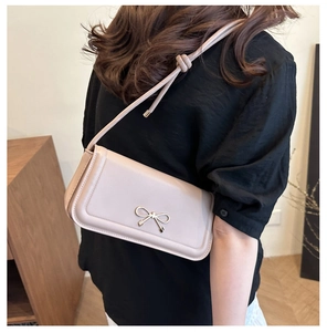 Detail of light beige underarm bag featuring a golden bow buckle and knotted shoulder strap