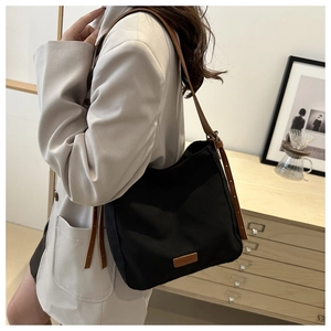 Détail du sac cabas en toile noire avec bandoulière en cuir marron et étiquette de marque