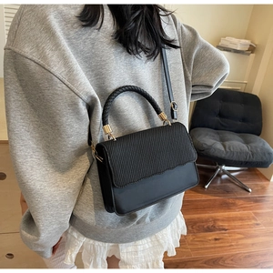 Detail of black crossbody bag with woven handle and wavy stitching on the flap cover