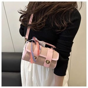 Detail of pink woven cylinder crossbody bag with lace bow and gold clasp on model