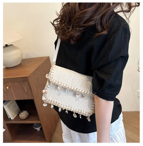 Close-up of straw woven crossbody bag with decorative shell tassels and long strap