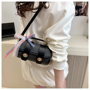 Détail du sac cylindrique noir avec texture tressée, fermoirs dorés et ruban dentelle