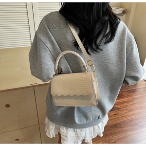 Detail of beige tote bag featuring woven texture flap and wavy cut edge on model shoulder