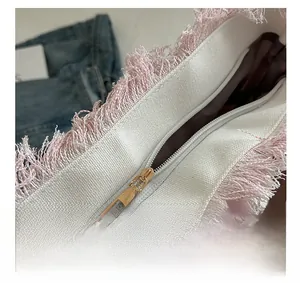 Details von rosa Quastenkanten und goldenem Reißverschluss an weißer Canvas-Tasche