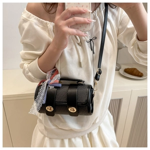 Détail du sac baril noir avec texture tissée, verrous dorés et nœud en ruban à carreaux